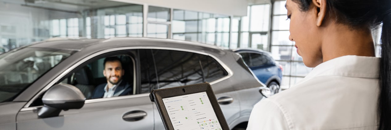 Buick Certified Service Representative Reviewing Vehicle Information on a Tablet with a Buick Owner in the Background